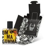 A square glass bottle of Ummagumma by Fzotic with a black cap is placed before its illustrated black-and-white box, offering an enticing adult gourmand perfume experience.