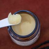 A jar of Cowboy & Co. COWGIRL Vanilla Infused Tallow, with some balm scooped onto a white spatula, sits against a reddish-brown background—perfect for nourishing sensitive skin.