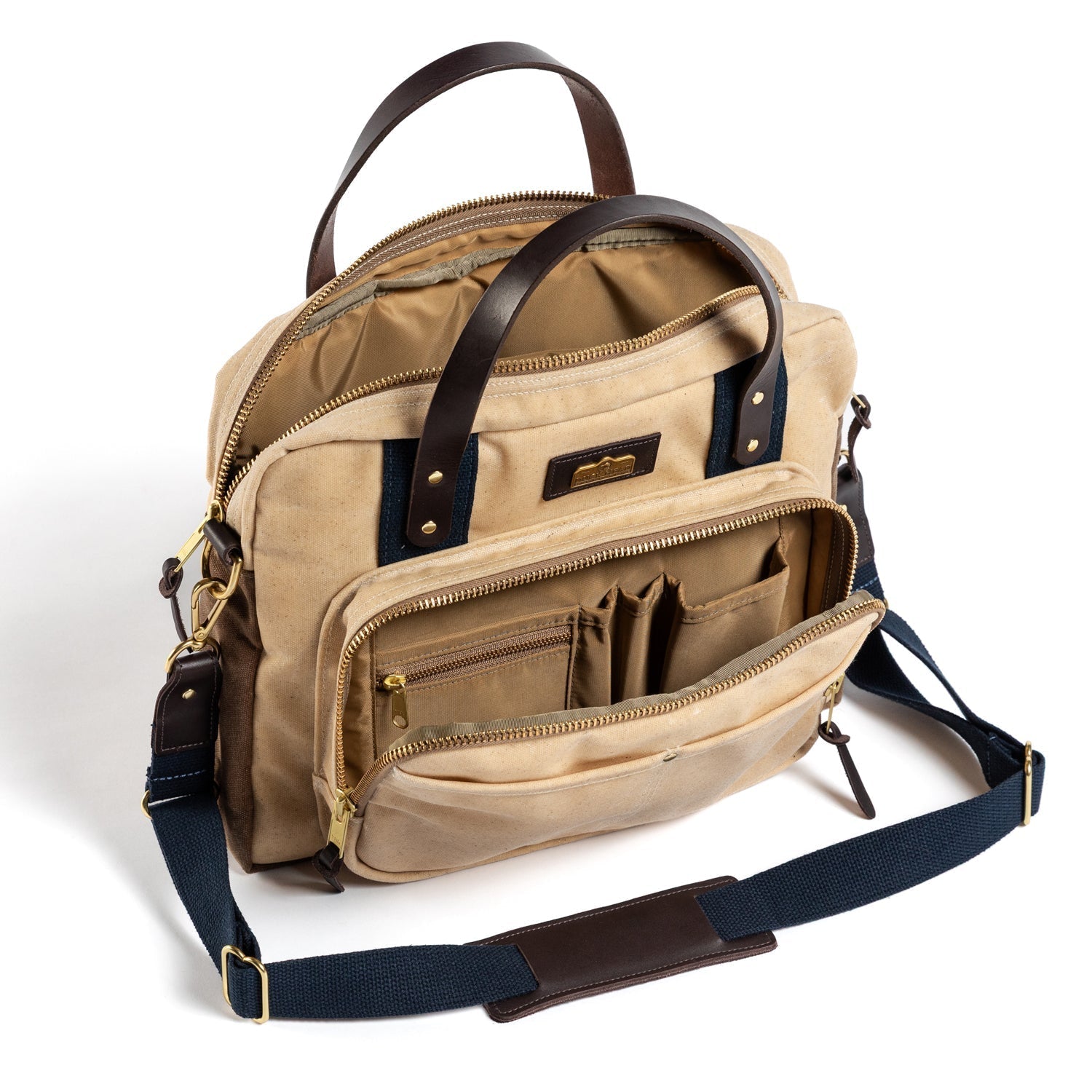 The Duck Head Waxed Canvas Laptop Bag features brown leather handles, a navy shoulder strap, multiple zippered compartments, interior organization, and a trolley sleeve. Made in the USA.