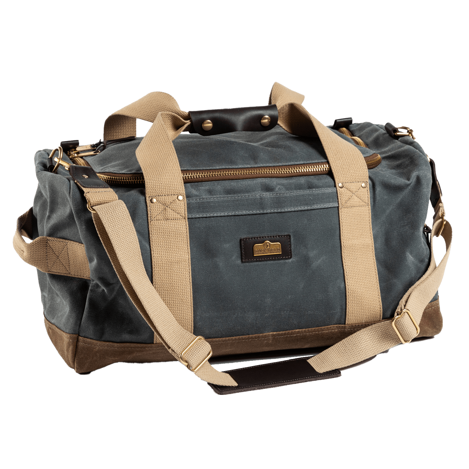 The Duck Head Waxed Canvas Overnighter Bag in charcoal, featuring tan straps, a front zipper pocket, brass hardware, and blue-gray and brown panels, is the perfect travel companion—made in the USA and shown on a white background.