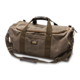 The Duck Head Waxed Canvas Weekender Bag features dark straps, a shoulder strap, brass hardware, and a front pocket. Carry-on compliant brown duffel shown against a plain white background.