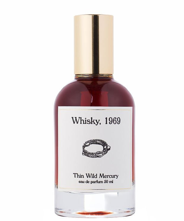 A 50ml bottle of Thin Wild Mercury’s Whisky eau de parfum, featuring a gold cap and white label with a chain design—evoking Sunset Strip rock club vibes and the smooth scent of bourbon.