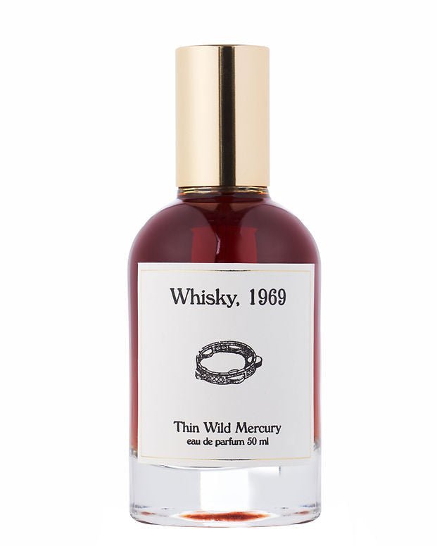 A 50ml bottle of Thin Wild Mercury’s Whisky eau de parfum, featuring a gold cap and white label with a chain design—evoking Sunset Strip rock club vibes and the smooth scent of bourbon.