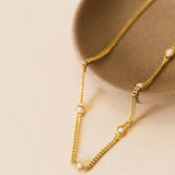 The JaxKelly White Opal Necklace—an 18k gold plated, hypoallergenic chain with small white opal stones—is displayed on the edge of a beige ceramic dish against a light background.