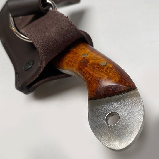 Close-up of the White Skunk Camp Knife by Woody Brand Knives, featuring a 1095 high carbon steel blade, wood handle, lanyard hole, and brown leather sheath. Proudly made in the USA.