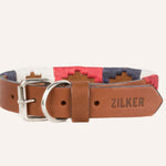 The Willie Dog Collar by Zilker Belts features hand-stitched brown leather, a silver buckle, and red, white, and blue embroidered fabric accents. "ZILKER" is embossed on the end for a stylish touch.