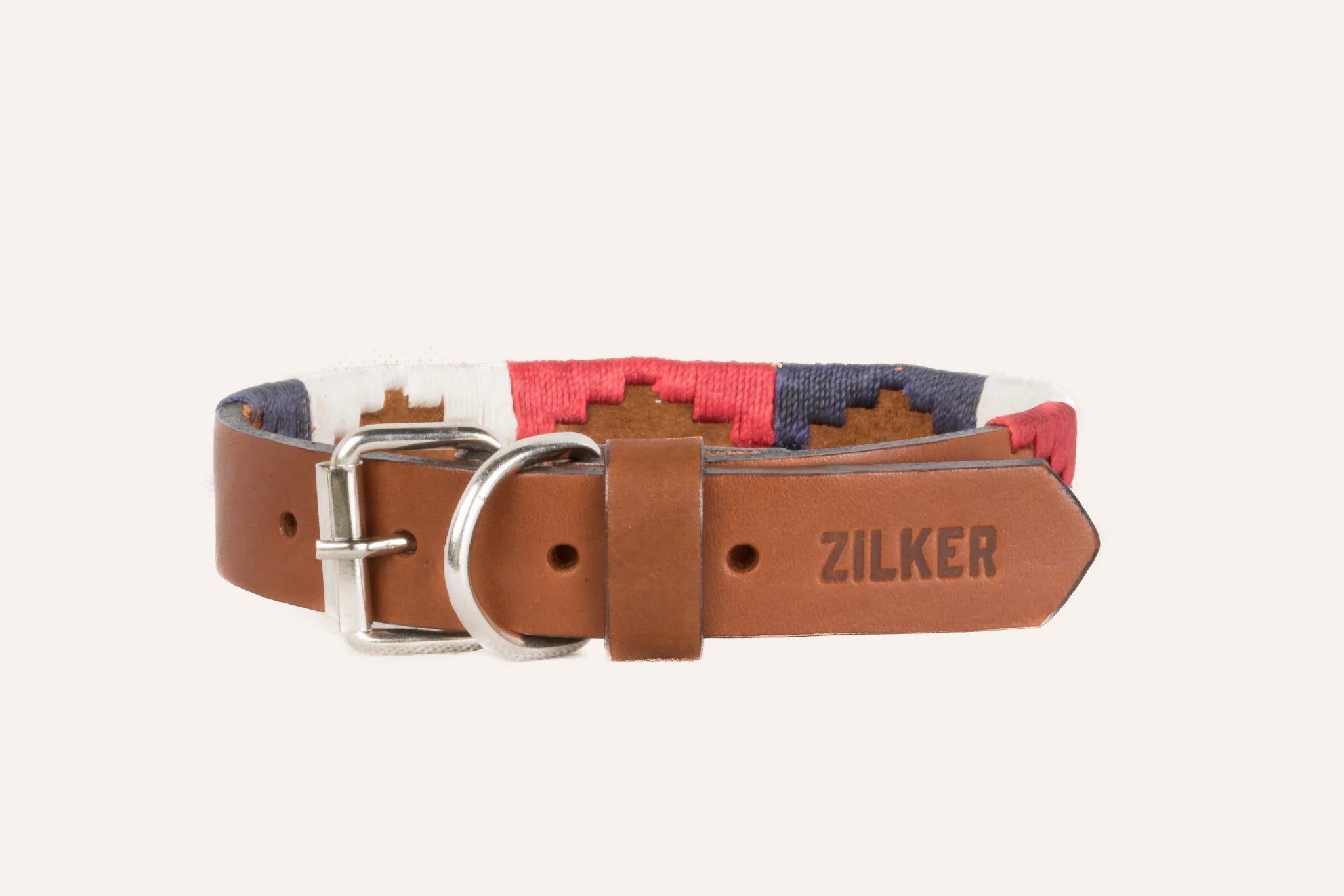 The Willie Dog Collar by Zilker Belts features hand-stitched brown leather, a silver buckle, and red, white, and blue embroidered fabric accents. "ZILKER" is embossed on the end for a stylish touch.