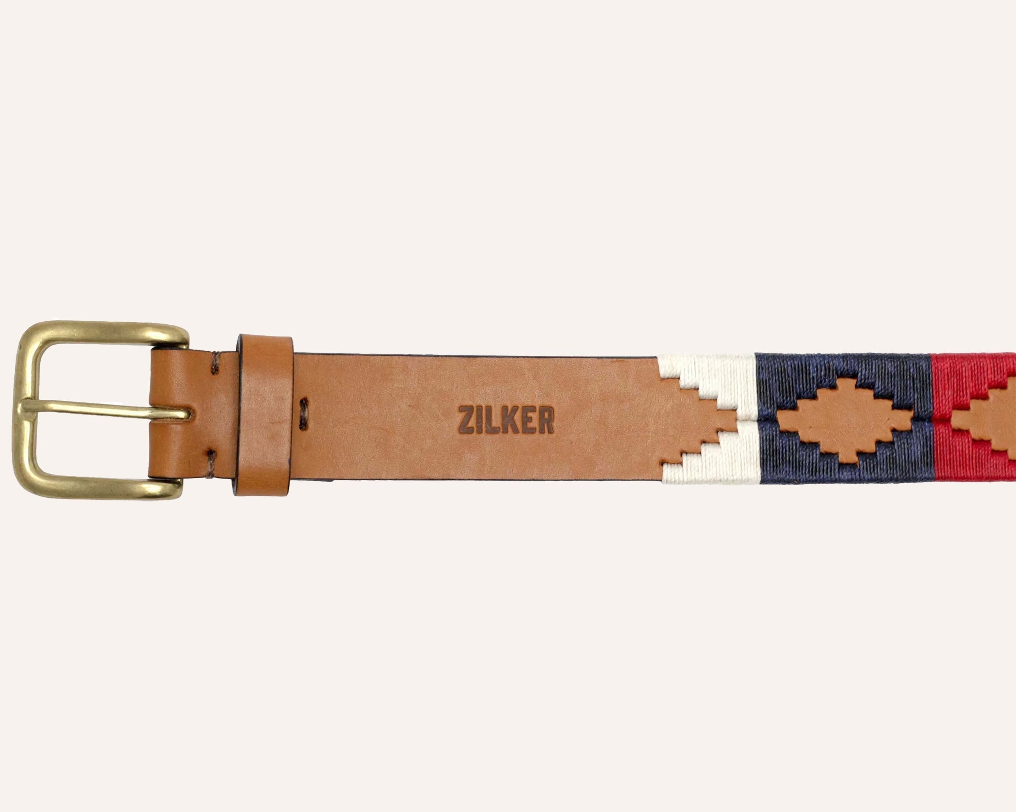 The Willie by Zilker Belts is a brown Argentine leather belt with a brass buckle, hand-stitched red, white, and navy geometric patterns, and "ZILKER" stamped at the center.