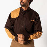 A man wears the Duck Head Woodland Shooting Shirt with tan recoil patches on the shoulder and elbows, paired with tan stretch twill pants, standing against a plain white background.