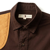 The Woodland Shooting Shirt by Duck Head is a brown stretch twill shirt with a quilted tan shoulder patch and an inner collar label displaying the Duck Head brand.