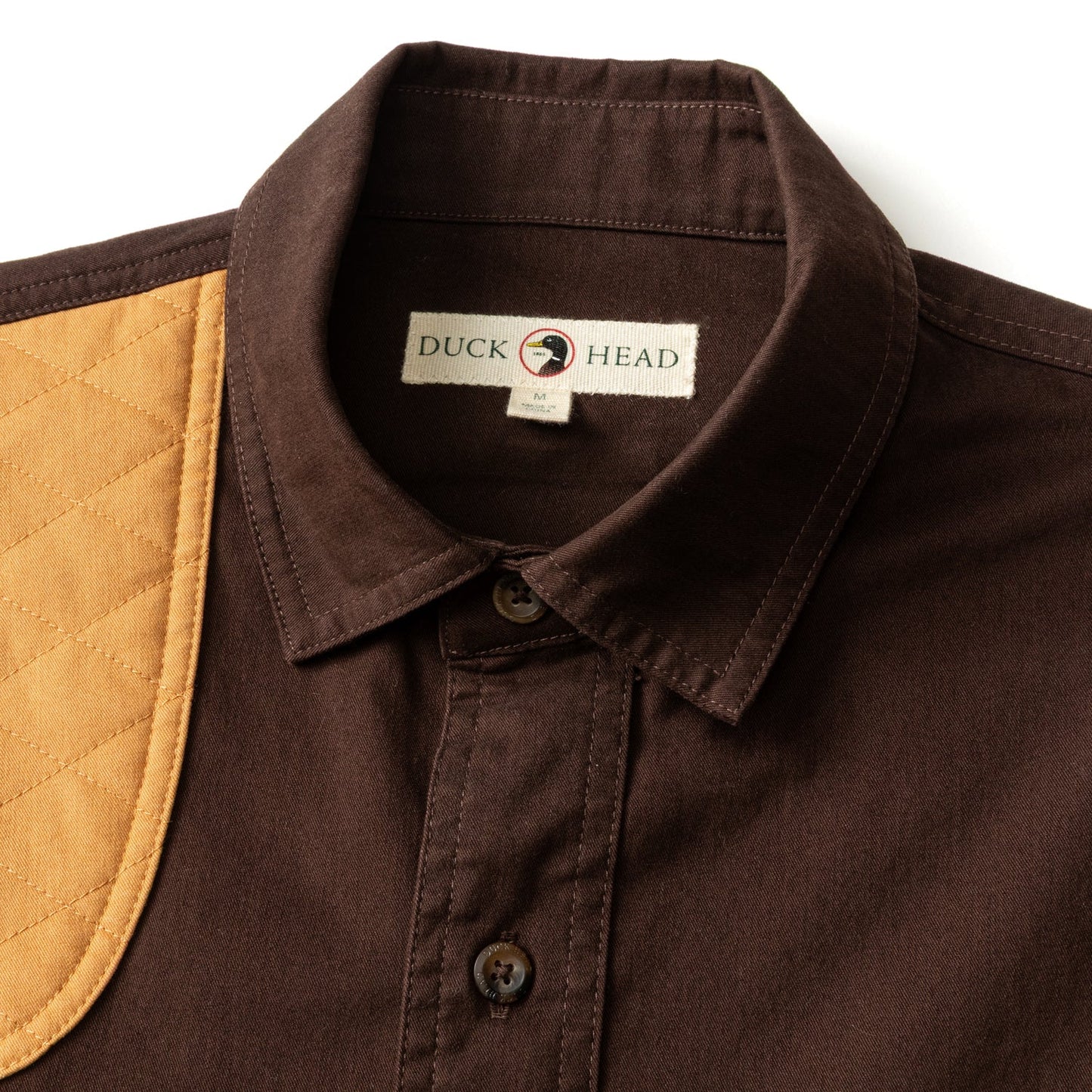 The Woodland Shooting Shirt by Duck Head is a brown stretch twill shirt with a quilted tan shoulder patch and an inner collar label displaying the Duck Head brand.