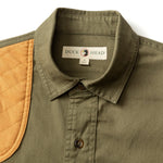 The Duck Head Woodland Shooting Shirt is an olive green stretch twill button-up with a quilted tan shoulder patch and a "Duck Head" label inside the collar.