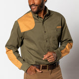 A man wearing the Duck Head Woodland Shooting Shirt, featuring olive green fabric and tan suede patches on the shoulders and elbows, stands against a plain background.