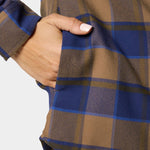A hand with manicured nails rests in the side pocket of the W's Campfire Shacket Pintail Plaid by Duck Camp, a brown and blue plaid shirt-style jacket.