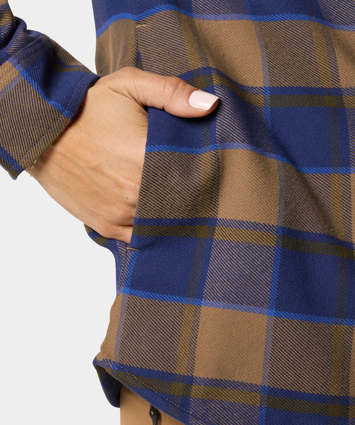 A person with neatly manicured nails places their hand in the pocket of a Duck Camp W's Campfire Shacket in Pintail Plaid.