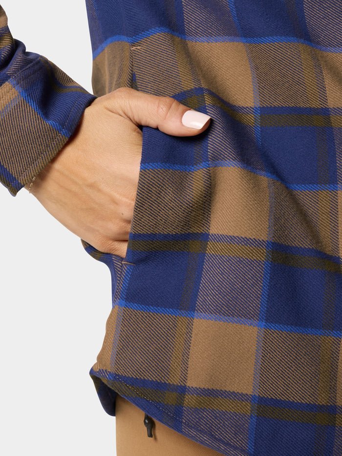 A hand with manicured nails rests in the side pocket of the W's Campfire Shacket Pintail Plaid by Duck Camp, a brown and blue plaid shirt-style jacket.