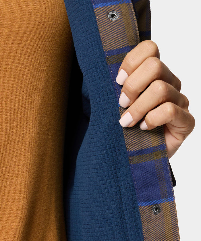 A person with light pink nail polish holds open a Duck Camp W's Campfire Shacket in Pintail Plaid, revealing a brown shirt underneath.