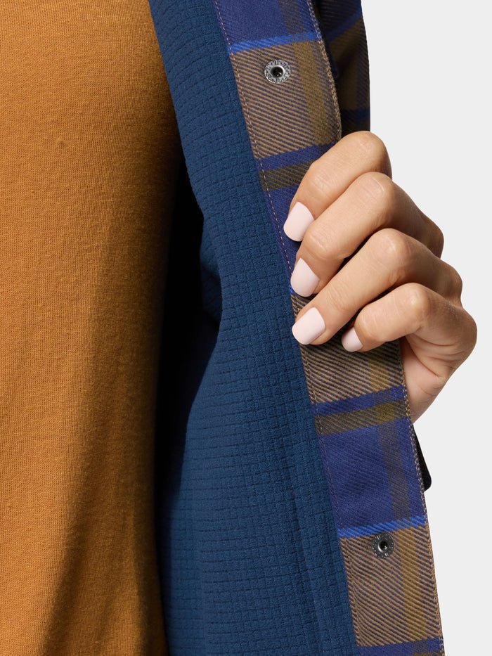 A person with light pink manicured nails holds open a Duck Camp W's Campfire Shacket in Pintail Plaid, revealing a brown top underneath.