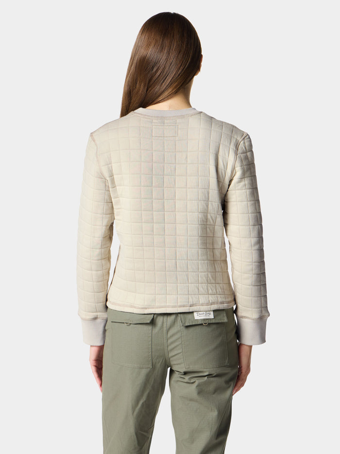 A person with long brown hair faces away, wearing the Duck Camp W's Cheyenne Quilted Crew and olive green pants—this quilted cotton crew neck sweater from Duck Camp is a comfy mid-layer ideal for everyday layering.