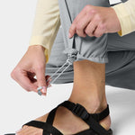 A person tightens the adjustable drawstring at the cuff of Duck Camp W's Gulf Pants in light gray while wearing black strap sandals.