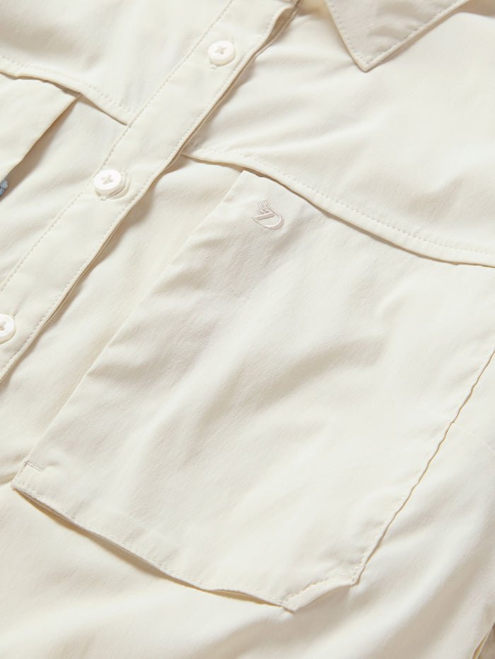 Close-up of the Duck Camp W's Lightweight Fishing Shirt Long Sleeve in light beige, featuring a chest pocket and a subtle embroidered logo above it.