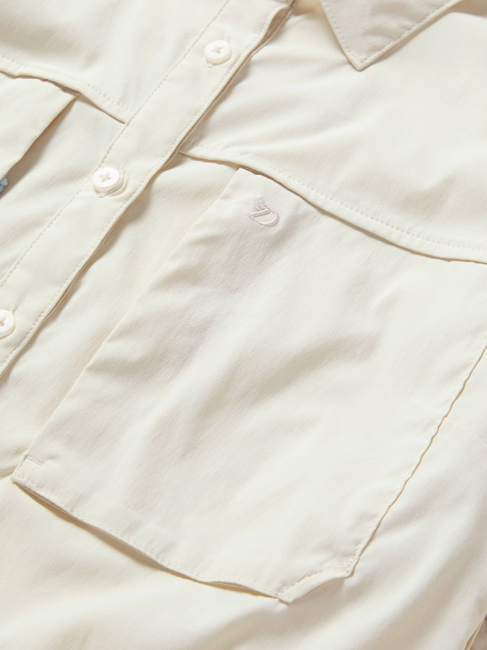 Close-up of Duck Camp W's Lightweight Fishing Shirt Long Sleeve in cream, featuring a chest pocket, buttons, collar, and small embroidered logo above the pocket.