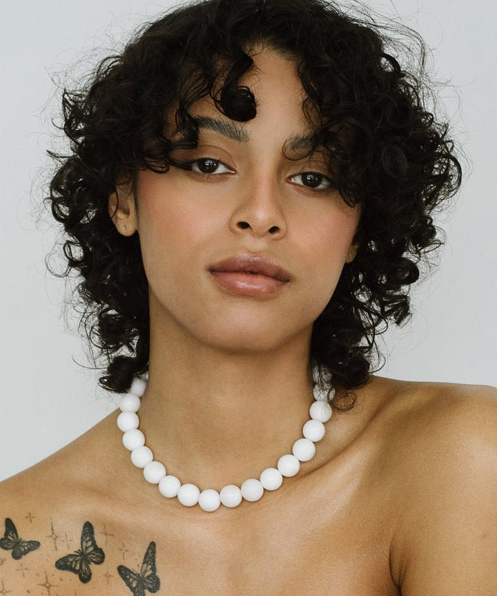 A woman with curly hair and butterfly tattoos on her shoulder models the Yona Collar by Kara Yoo, posing in a Vancouver studio against a plain background.