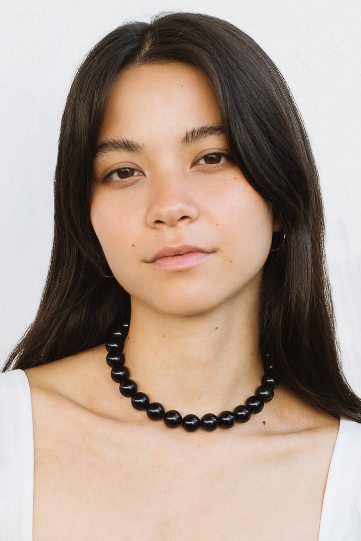 A woman with long dark hair wears the Yona Collar by Kara Yoo and a white top, standing against a plain light background in a Vancouver studio.