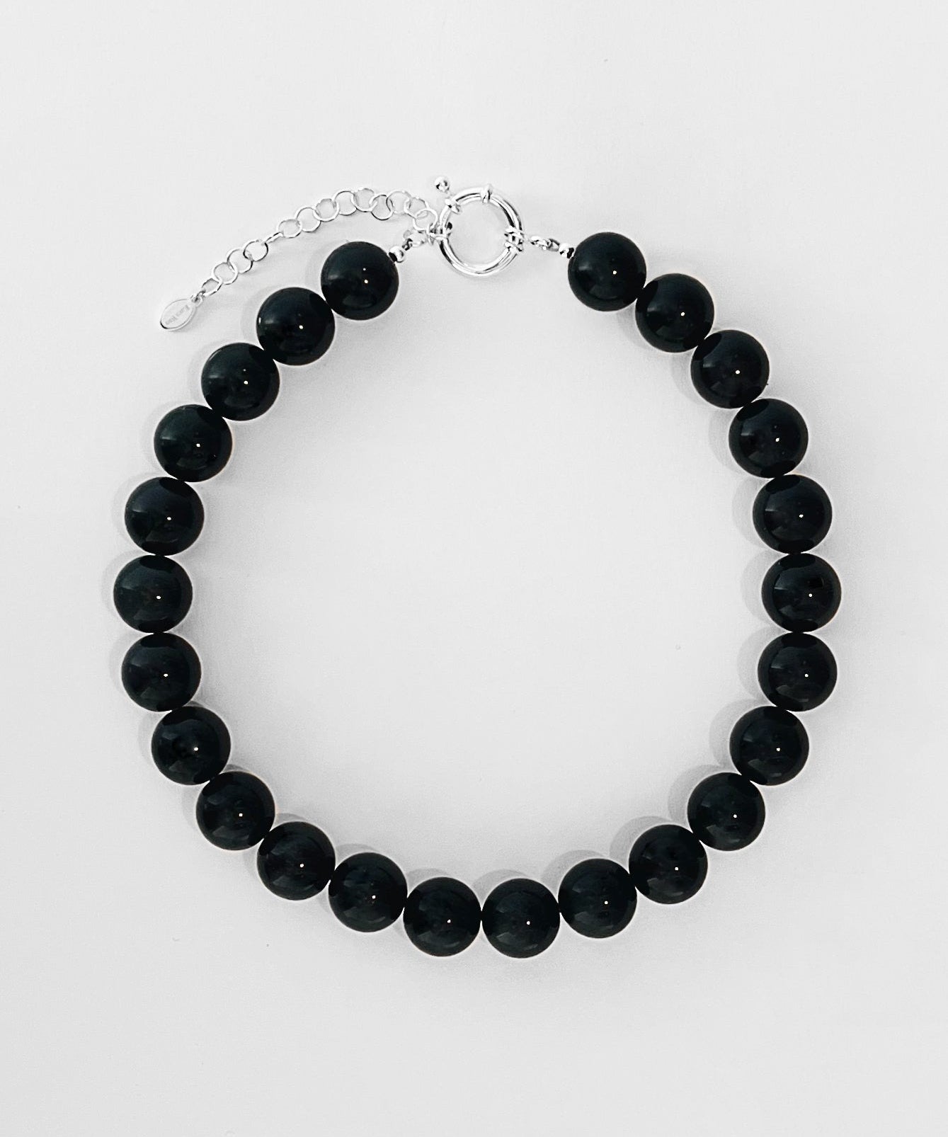 The Yona Collar by Kara Yoo features round black beads and a silver adjustable chain with clasp, crafted in Vancouver, shown arranged in a circle on a white background.