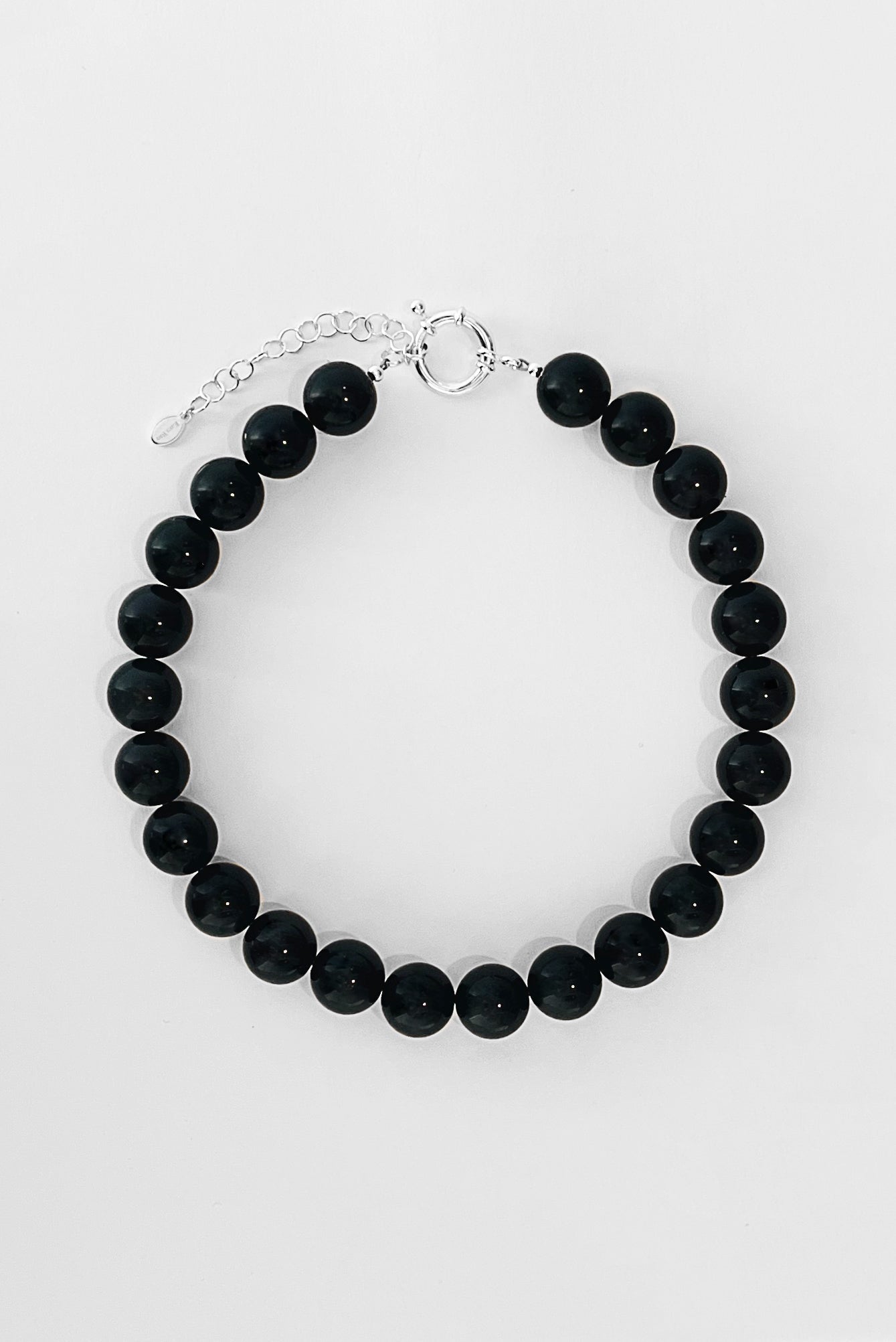 The Yona Collar by Kara Yoo features round black beads and a silver adjustable chain with clasp, crafted in Vancouver, shown arranged in a circle on a white background.