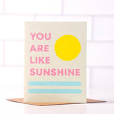 The "You Are My Sunshine" A2 greeting card by Daydream Prints features pink text, a yellow sun, and blue lines on eco-friendly stock with a recycled brown envelope. Designed in Portland, Oregon.