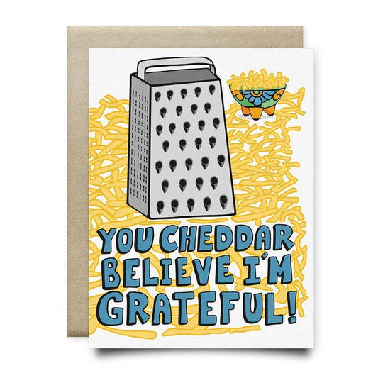 The "You Cheddar Believe I'm Grateful - Thank You Card" by Anvil Cards features a hand-drawn cheese grater, grated cheese, and the punny message on shredded cheese—printed on sustainable linen paper. A2 size, blank inside.