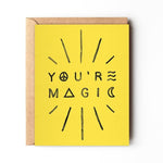 A yellow "YOU'RE MAGIC" greeting card with black text and radiating lines from Daydream Prints, paired with a recycled envelope. Made in Portland.