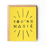 A yellow "YOU'RE MAGIC" greeting card with black text and radiating lines from Daydream Prints, paired with a recycled envelope. Made in Portland.