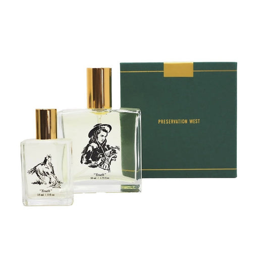 Two clear perfume bottles with gold caps and black illustrations sit beside a green and gold box labeled "Youth" by Preservation West.