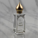 The Nemat Amber Eau de Parfum Spray 50ml features a clear bottle with a gold cap, displayed on a marble surface—an ideal signature scent from the brand Nemat.