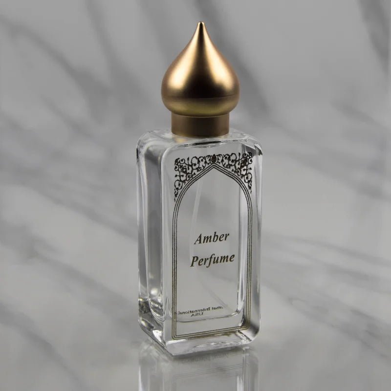 A clear glass bottle labeled "Amber Eau de Parfum Spray 50ml | Nemat" with a gold pointed cap sits against a light gray marble background, reflecting the elegance of Nemat’s amber fragrance.