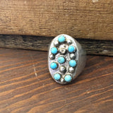 The Vintage 8-Stone Turquoise Studded Ring features an oval face with turquoise stones and silver beads set on a sterling silver band, size 13.5, beautifully displayed on a wooden surface.