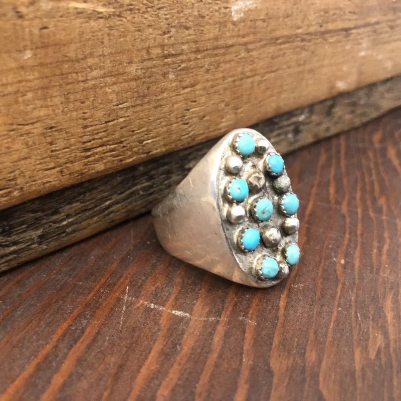 The Vintage 8-Stone Turquoise Studded Ring features a sterling silver oval face with turquoise stones and silver beads, elegantly crafted in size 13.5—an ideal unique accessory displayed on a wooden surface.