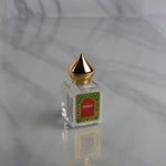 A glass Amber Perfume Oil bottle by Nemat, featuring a gold pointed cap and a decorative "Amber" label, sits on a reflective marble surface, capturing the allure of this signature Nemat fragrance.