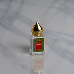 Amber Perfume Oil by Nemat features a small glass bottle with a gold pointed cap and red "Amber" label, set on gray marble. This subtle fragrance enhances your unique scent.
