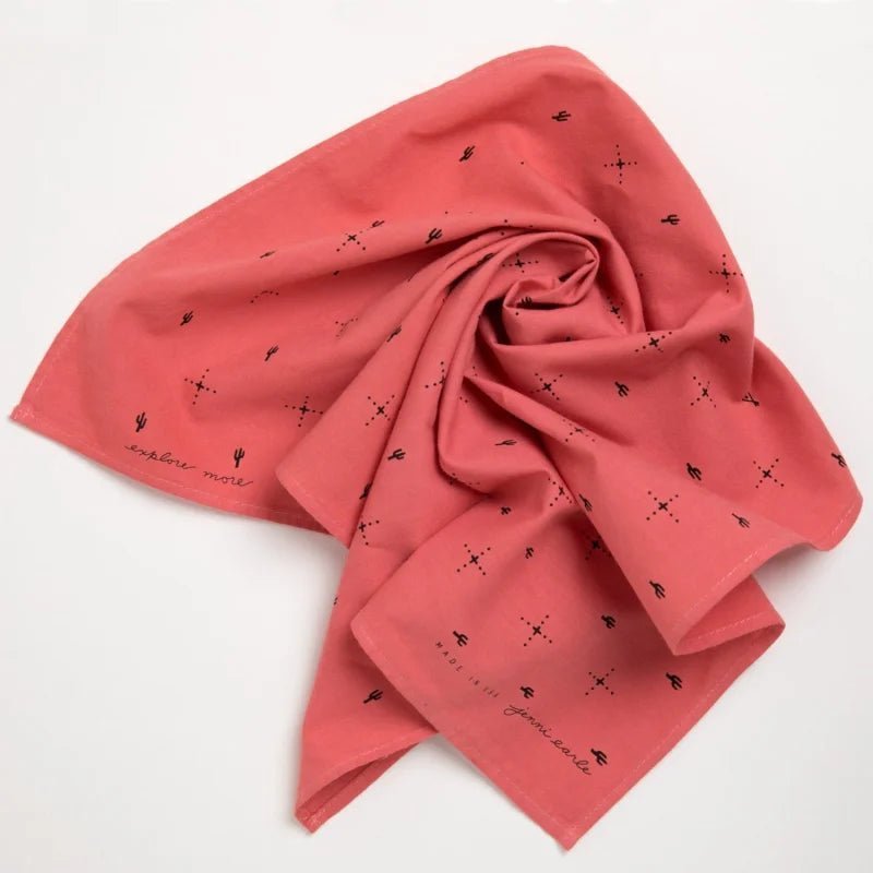 The Jenni Earle "Explore More" Bandana features hand-dyed salmon cotton with black geometric and cactus motifs and “explore more” in cursive on the corner, shown flat against a white background.
