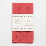 The “Bandana | Explore More” by Jenni Earle is a folded, hand-dyed red cotton bandana with small black geometric and animal motifs, wrapped in a white paper label featuring text and arrow graphics.