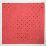 The Jenni Earle "Explore More" bandana features a red hand-dyed cotton fabric with small black dots and symbol patterns, evenly spaced for an adventurous look.