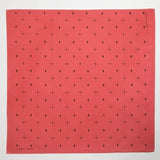 The Jenni Earle "Explore More" bandana features a red hand-dyed cotton fabric with small black dots and symbol patterns, evenly spaced for an adventurous look.
