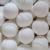 A close-up of Old Whaling Co.'s Coconut Milk Bath Bombs shows several round, white spheres stacked together, each with a visible seam and infused with epsom salts for a soothing soak.