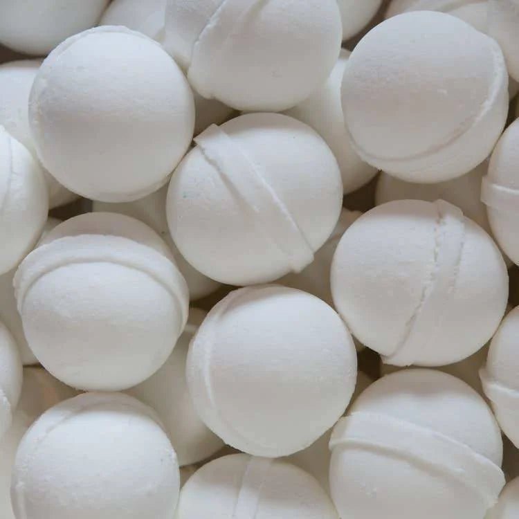 A close-up of Old Whaling Co.'s Coconut Milk Bath Bombs shows several round, white spheres stacked together, each with a visible seam and infused with epsom salts for a soothing soak.