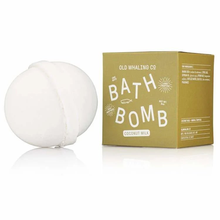 A white bath bomb with epsom salts rests by a green "Bath Bomb | Coconut Milk | Old Whaling Co." box from Old Whaling Co., offering a soothing soak.