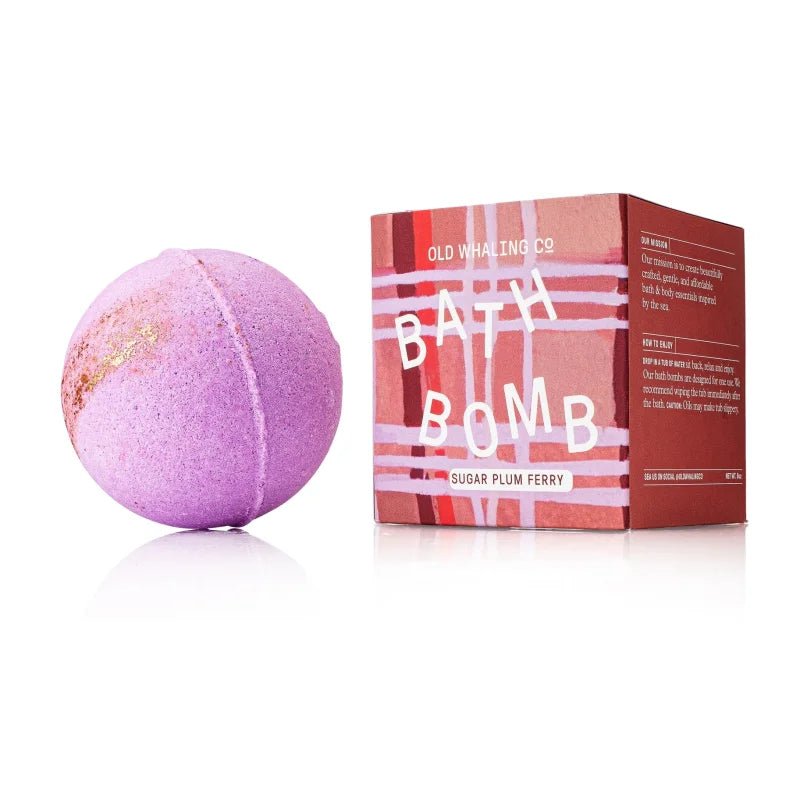 A purple Bath Bomb | Sugar Plum Ferry by Old Whaling Co. with moisturizing epsom salts sits beside a red Old Whaling Co. box.