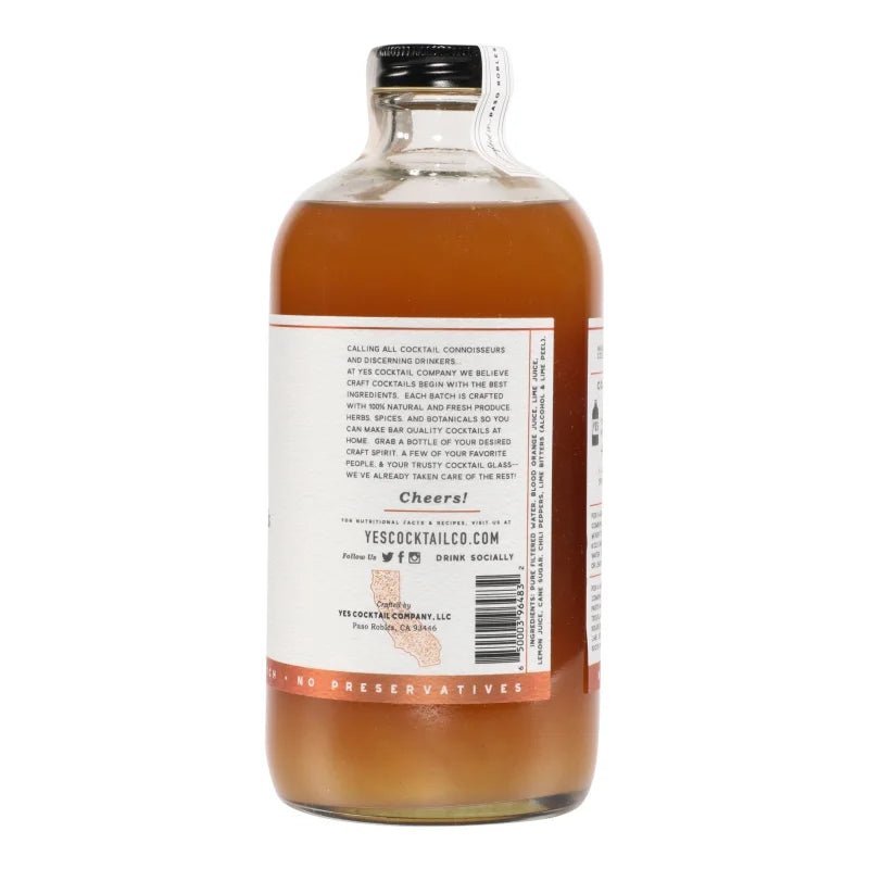 A clear glass bottle of Yes Cocktail Co. Blood Orange & Chili Pepper Cocktail Mixer, featuring a back label with text and website and capped with a black top—perfect for crafting a spicy margarita.